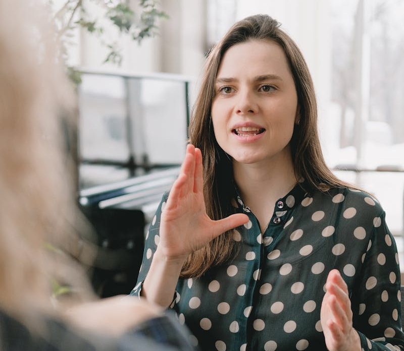 Focused woman in a polka dot blouse engages in a conversation indoors.
